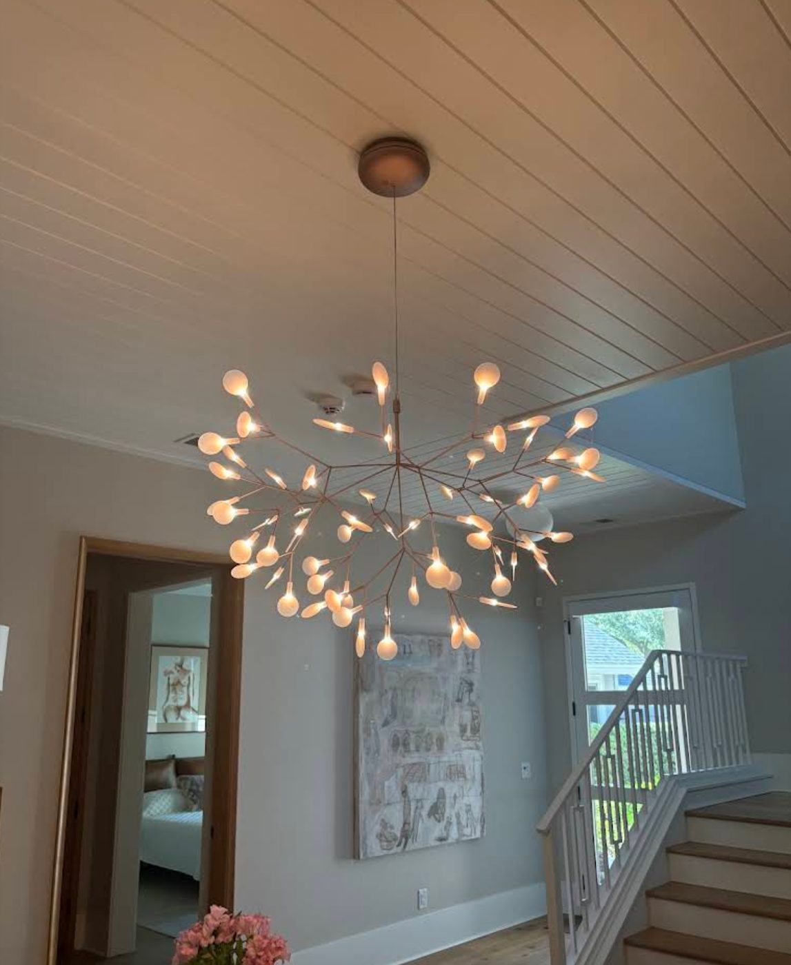 Large branching chandelier with dozens of bud-shaped lamps hung below a shiplap ceiling in a home entry